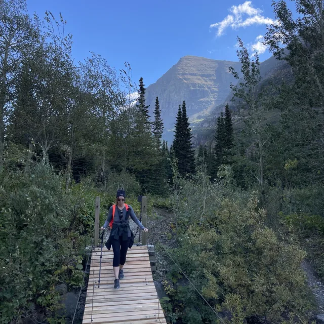 Travel Advisor Kathy Potter hiking across a bridge with mountains and green shrubs around.