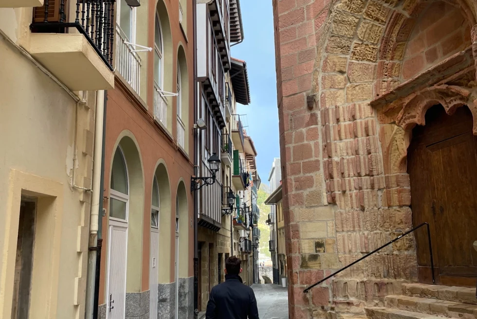 a man in a black coat walks down a narrow cobblestone street in day