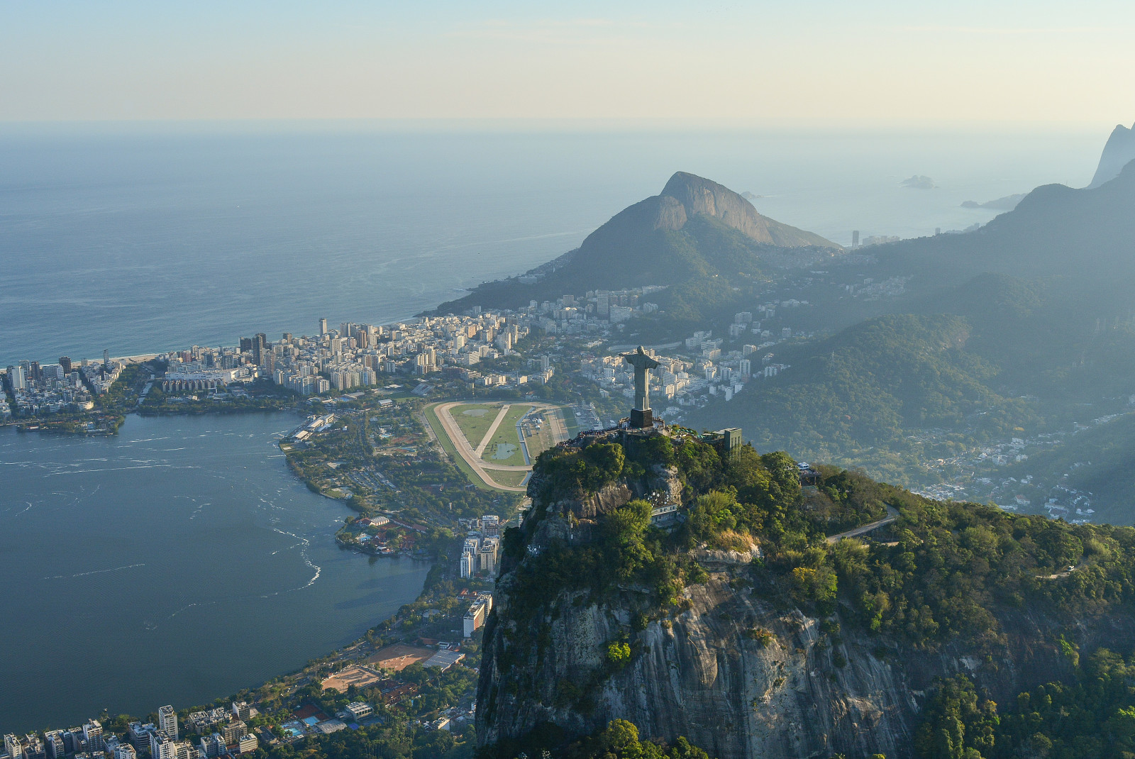 Mountain with statue on top overlooking a body of water during daytime