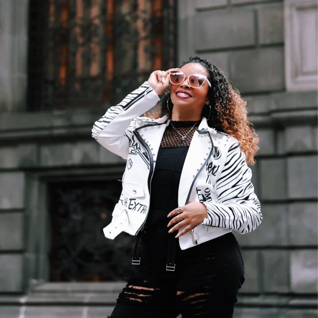 Travel Advisor Kristina Daferede in a white and black jacket with rose glasses in front of stone brick.
