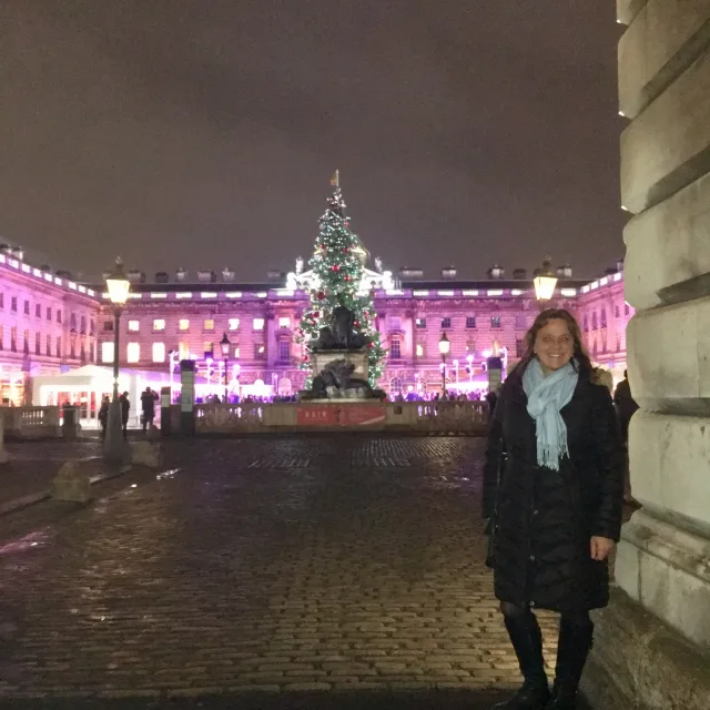 woman in a black coat standing in front of a palace lit up in pink