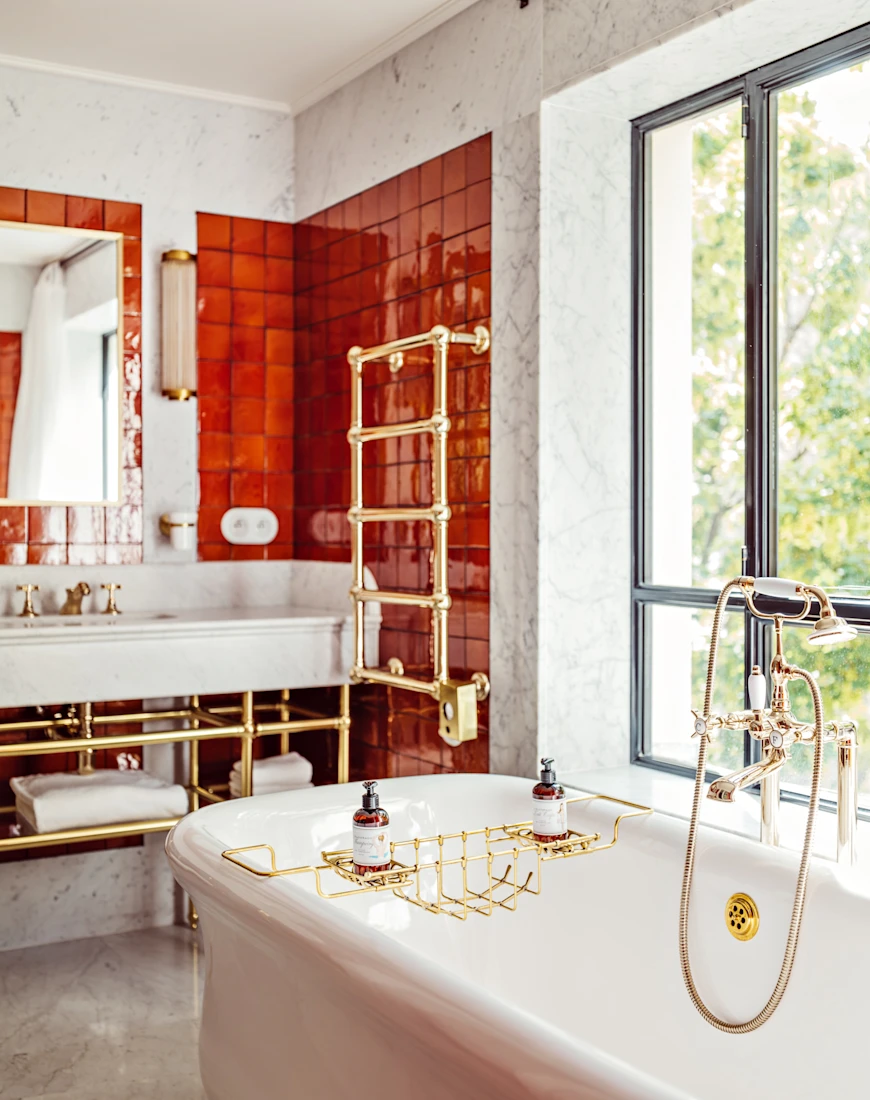 a luxe bathroom with red wall tiles and a large white tub near a big sunny window
