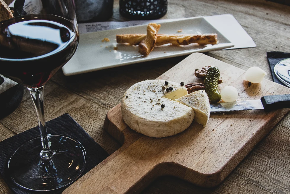 A glass of red wine, cheese and pickles on a wooden plate. 