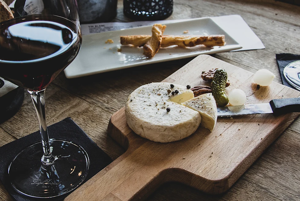 A glass of red wine, cheese and pickles on a wooden plate.