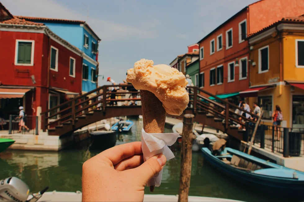 hand holding up a cone of gelato in front of a canal