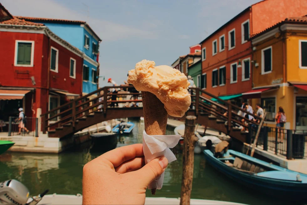 hand holding up a cone of gelato in front of a canal