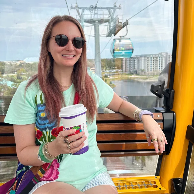 Travel advisor Laura Davidson in a green top and sunglasses with a hot drink in hand posing on a cable car