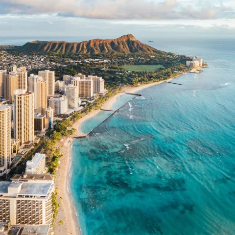 A drone-shot of Waikiki's coastline, skyline, beach, and mountains.