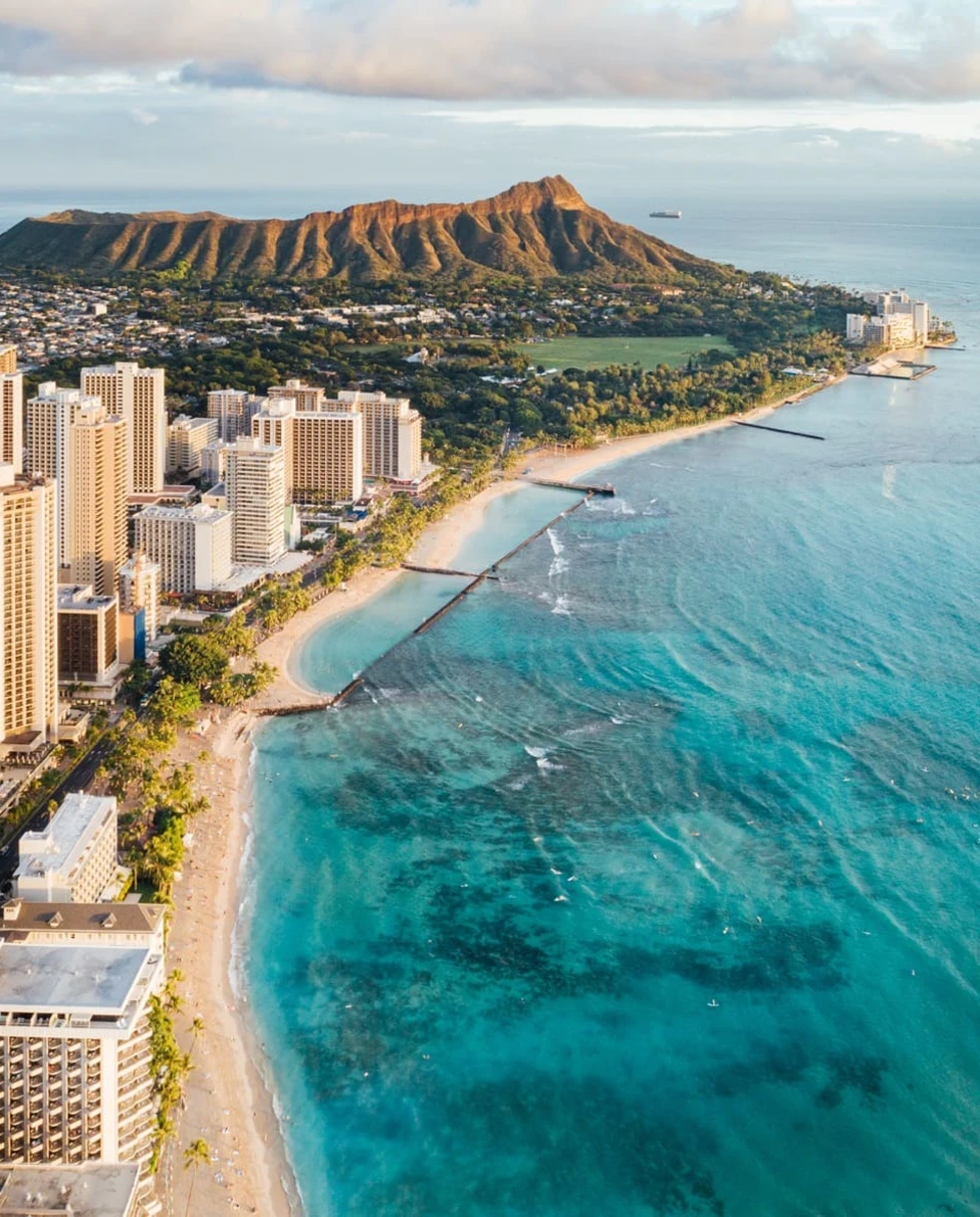 A drone-shot of Waikiki's coastline, skyline, beach, and mountains.