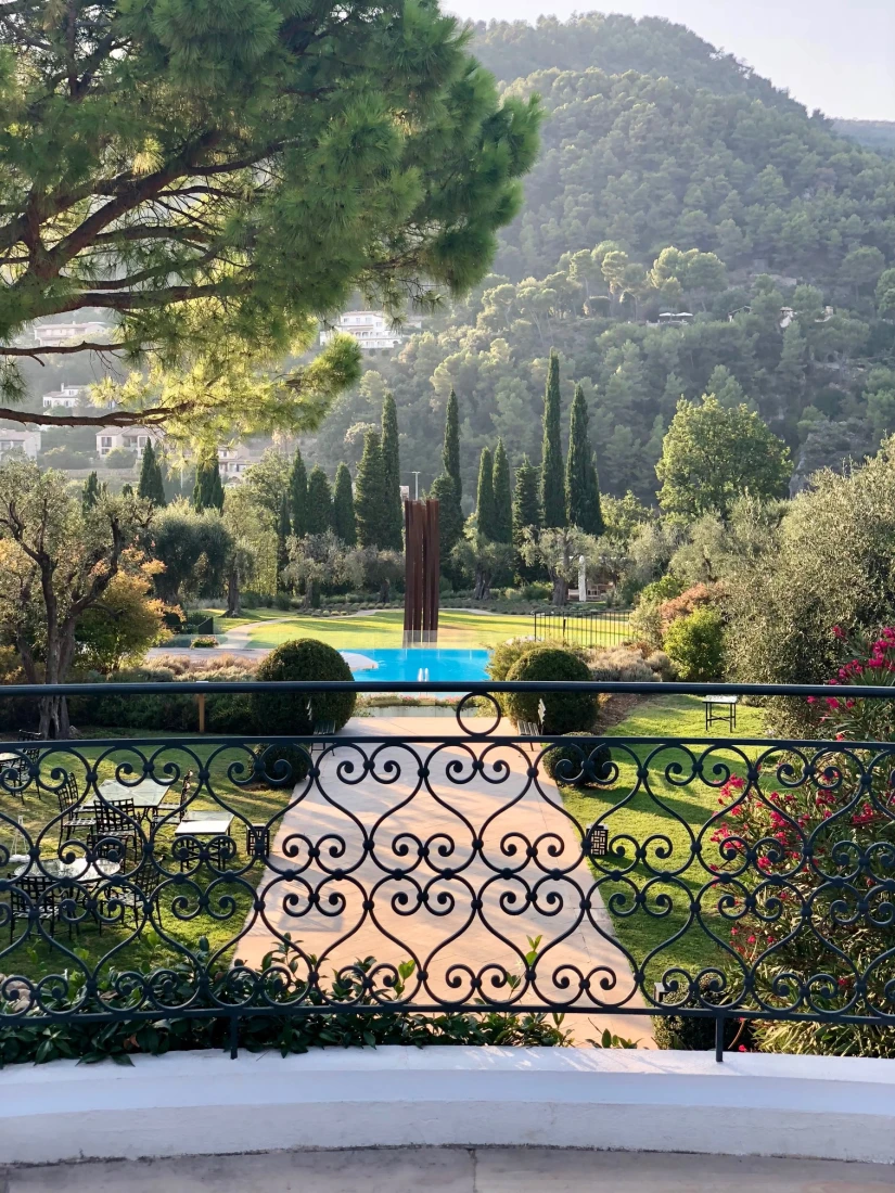 View of the ChateauPool from behind an iron railing on a balcony, with wooded hills in the distance