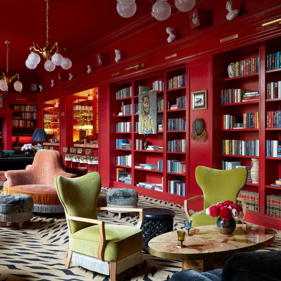 A room with built in book shelves in red walls and green and pink chairs.