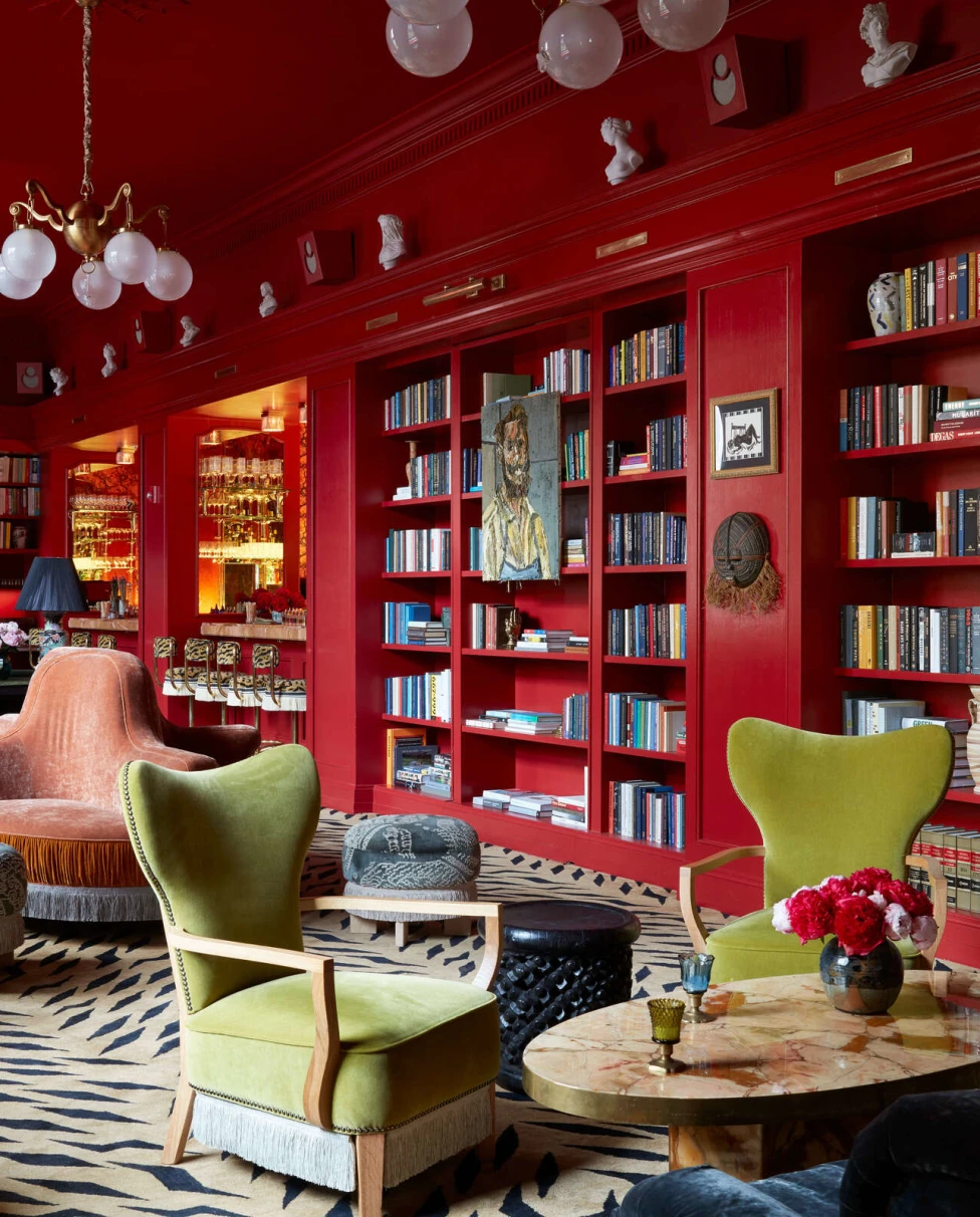 A room with built in book shelves in red walls and green and pink chairs.