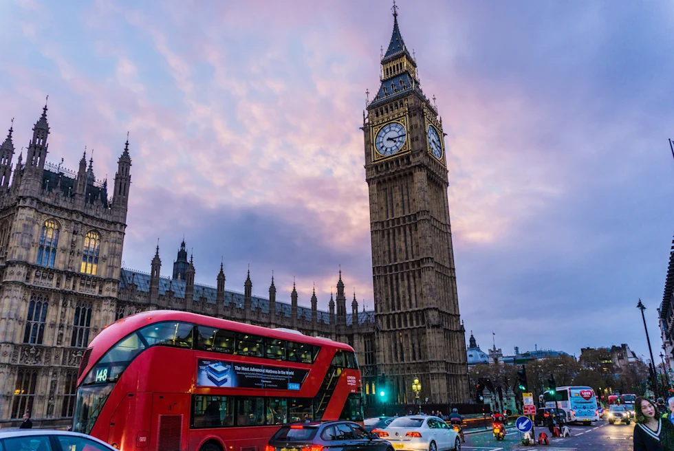 Clock tower with a red double decker in front.