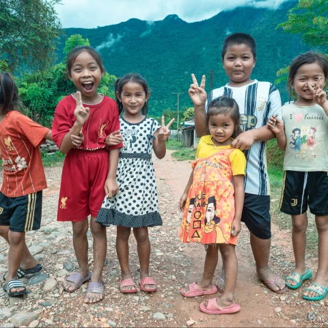 A group of kids posing with victory sign outside. 