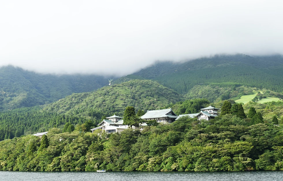white temple sitting on green hills in Japan with a lake in front and low white clouds