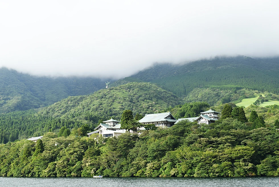 white temple sitting on green hills in Japan with a lake in front and low white clouds