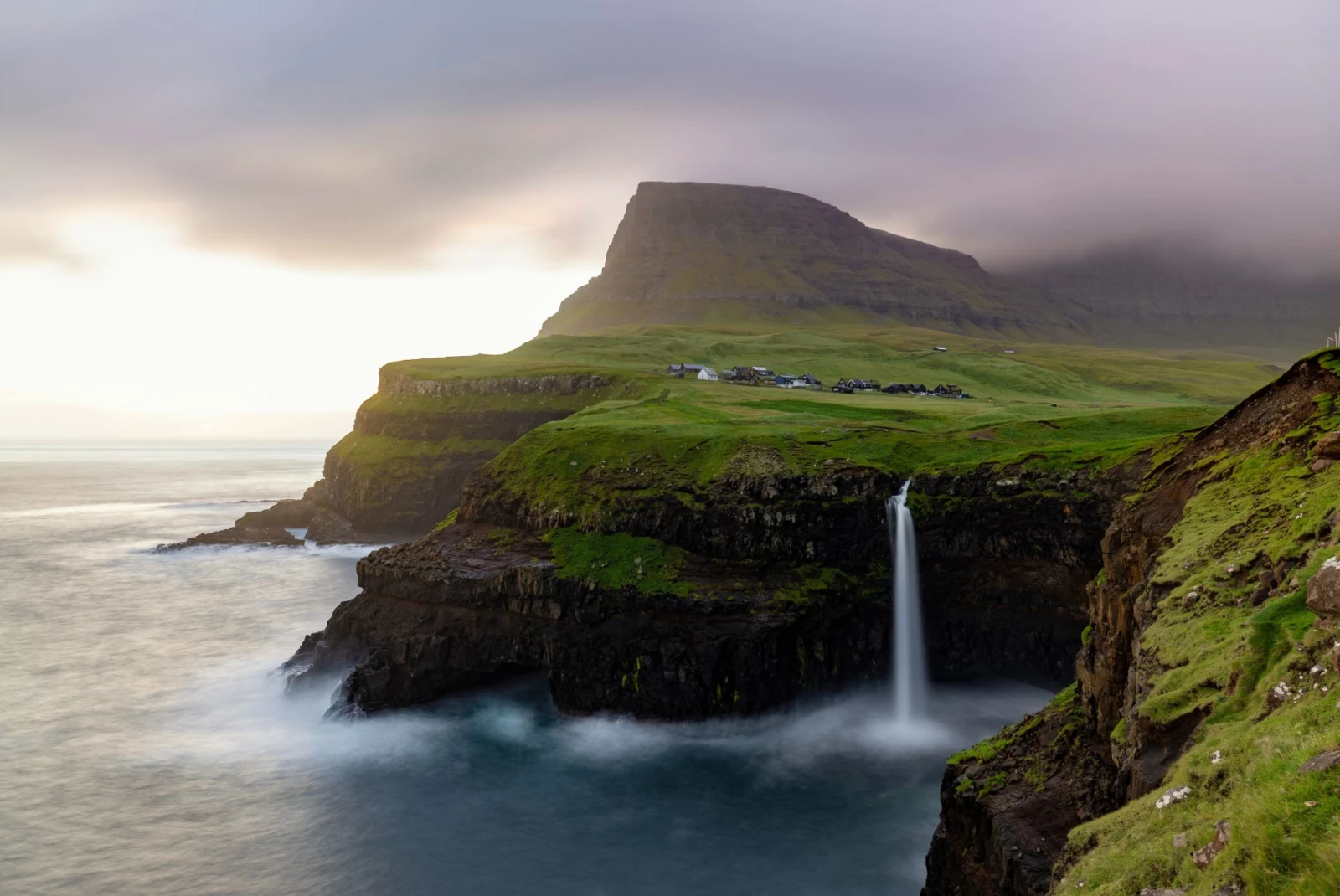 dramatic single waterfall off a grassy cliff into the ocean on a cloudy day at sundown