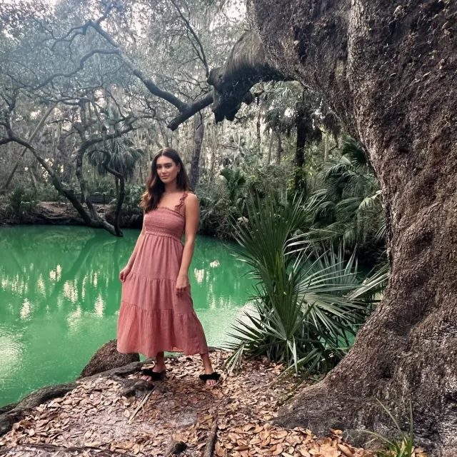 Picture of Annemarie wearing a pink dress near a green lagoon and large tree.