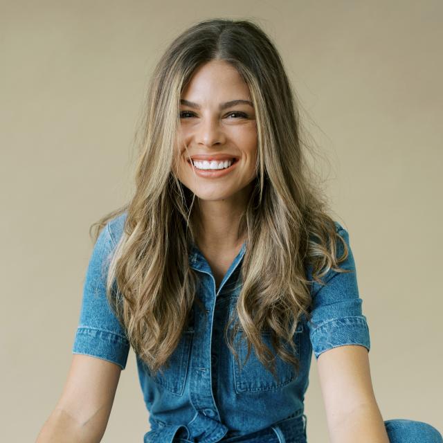 Fora travel agent Elizabeth Jones wearing jean shirt with tan backdrop