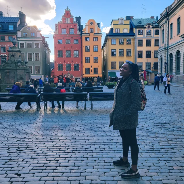 Travel advisor Tiffany Giles stands in a cobblestoned square near colorful buildings wearing a green jacket