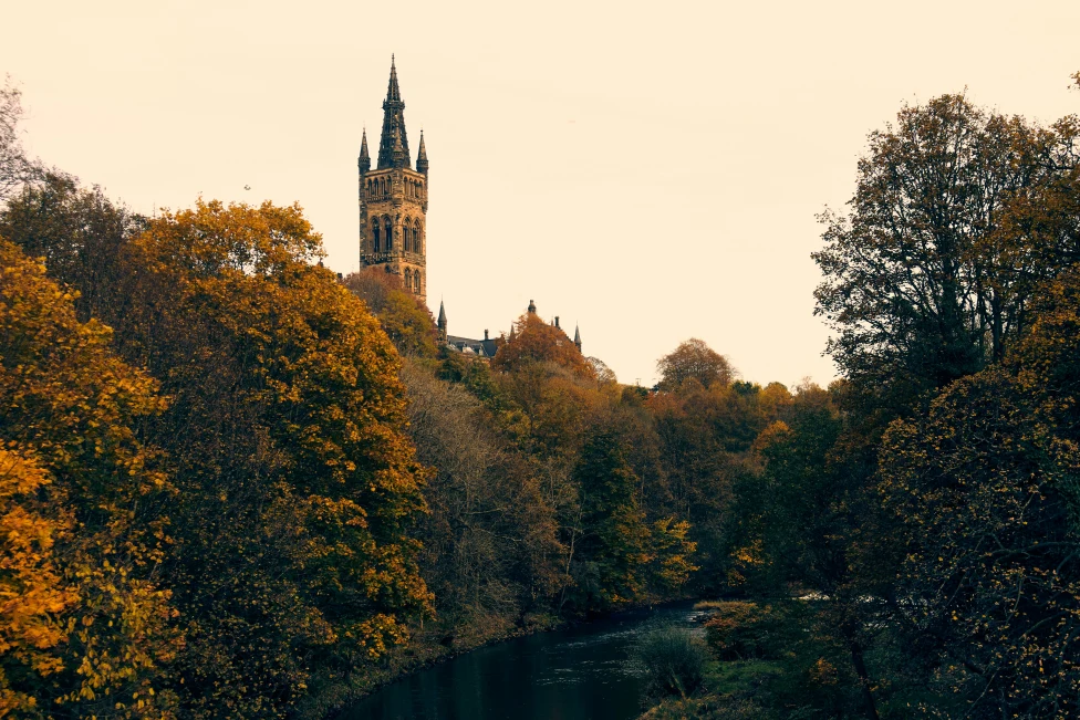 A cathedral spire on a hillside next to a river with trees at sunset in Glasgow.