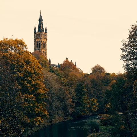 A cathedral spire on a hillside next to a river with trees at sunset in Glasgow.