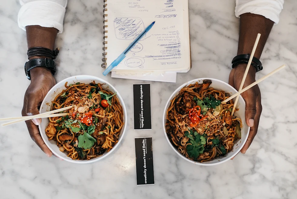 A black woman holding two bowls of noodles.