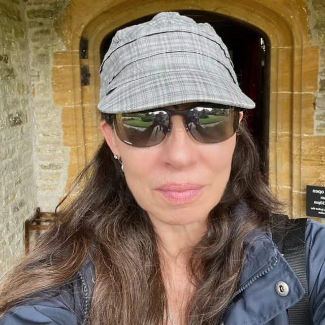 Shery posing for a selfie wearing a hat and sunglasses in front of a stone doorframe