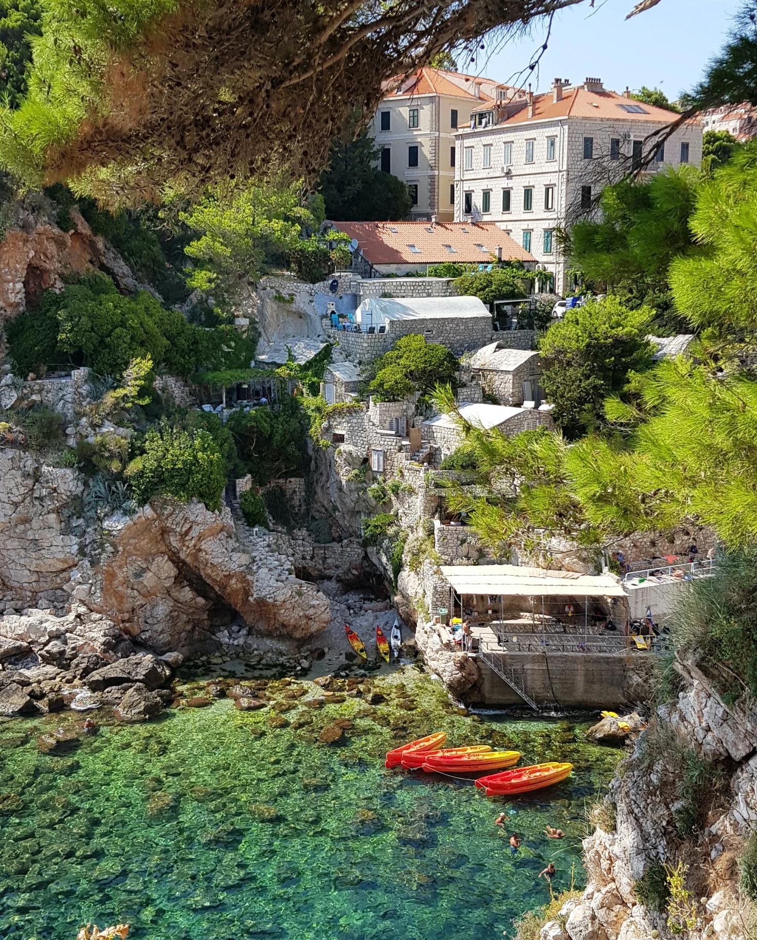 rocky cliff with buildings into clear waters with kayaks 