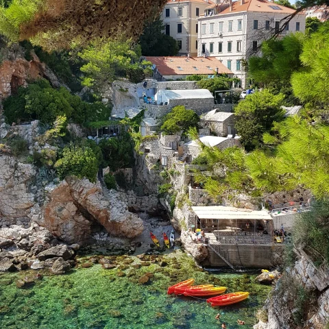 rocky cliff with buildings into clear waters with kayaks 