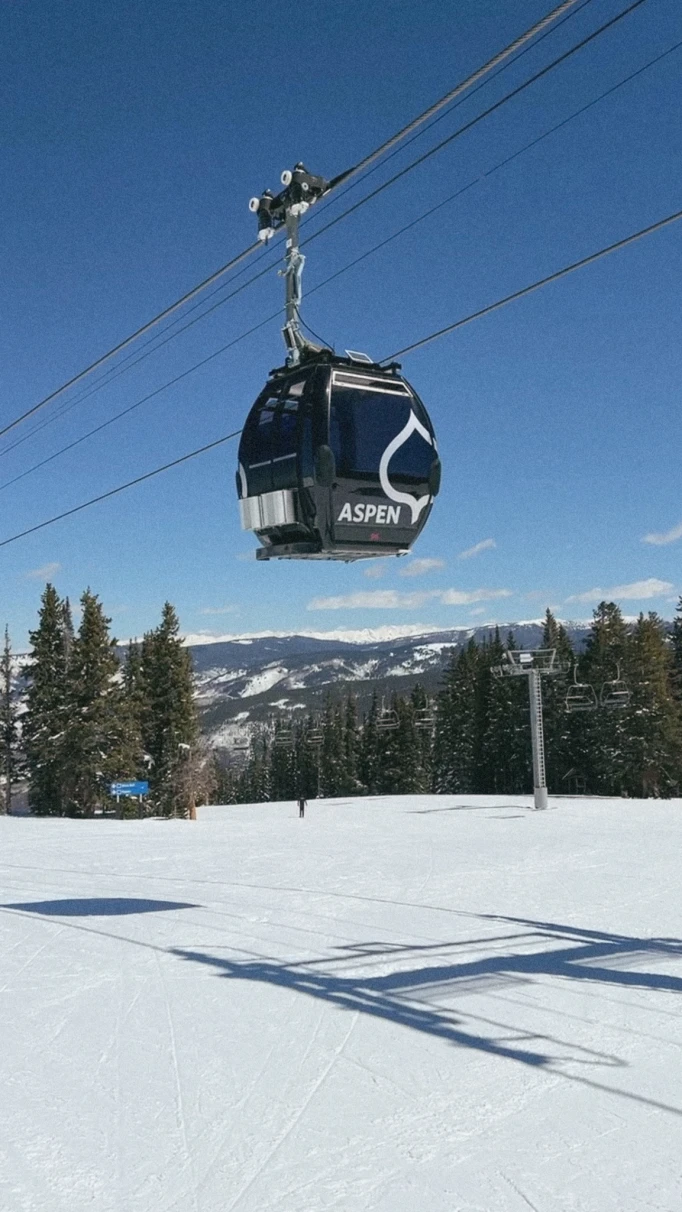 A gondola style ski lift above the snow, mountains, and frosted trees. 