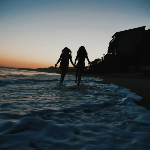 A picture of silhouette of two women running across seashore.