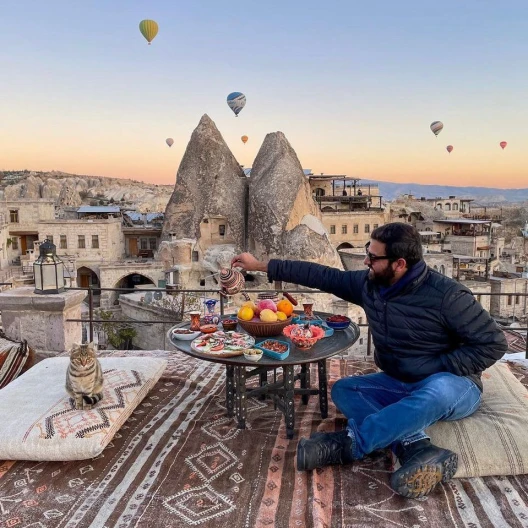 man enjoying a rooftop picnic on a terrace overlooking a sky dotted with hot air balloons