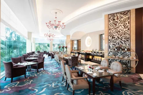 A dining room at the Shangri-La Singapore, with a buffet, red chandeliers and floor-to-ceiling windows overlooking trees.
