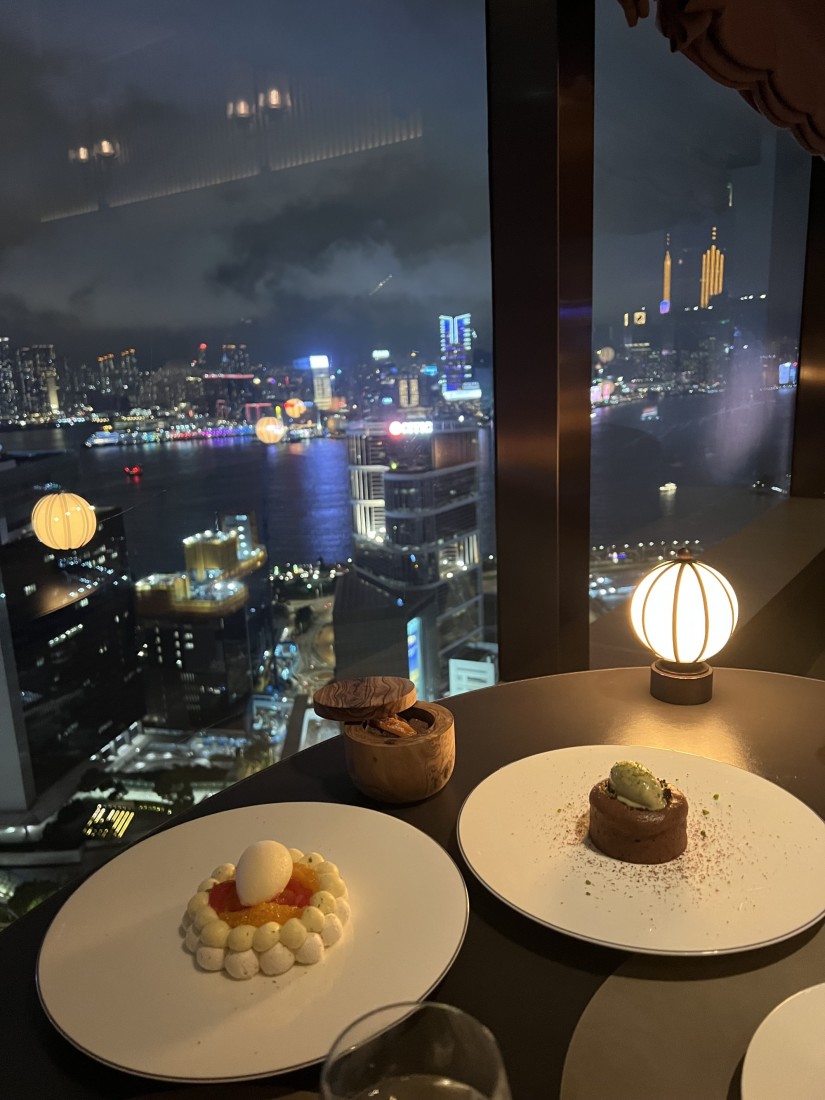 Perfectly designed desserts placed on a table, in front of windows with a view of Hong Kong lit up at night.