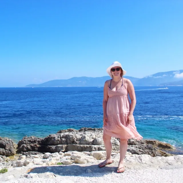 Travel advisor posing on the beachside in a pink dress and a hat 
