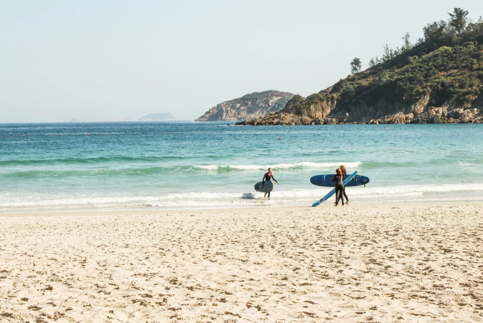 beach with islands in the distance and three surfers with surf boards on the beach