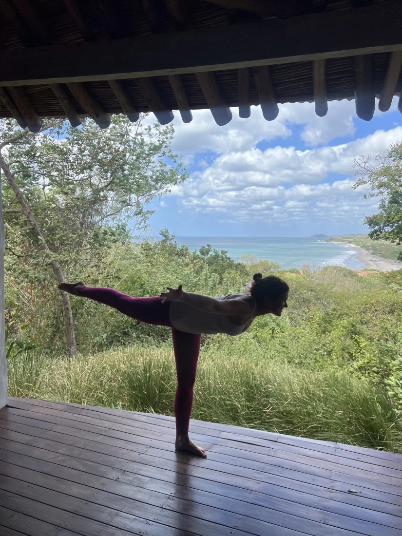 Travel advisor Emily in a yoga pose on a wooden deck overlooking a beautiful view of green foliage and the beach in the distance.