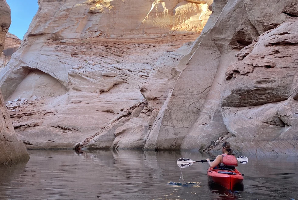 Woman in red kayak in body of water next to large rocks during daytime