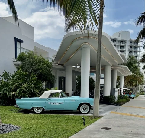 entrance to the hotel with a classic car parked in front with palm trees