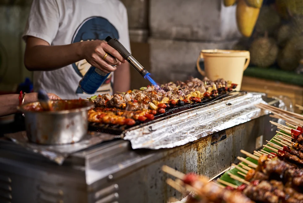 Street vendor in Thailand blow torching chicken on grill