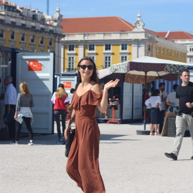 travel advisor Carli Pisano wears a brown jumpsuit and waves in the city square