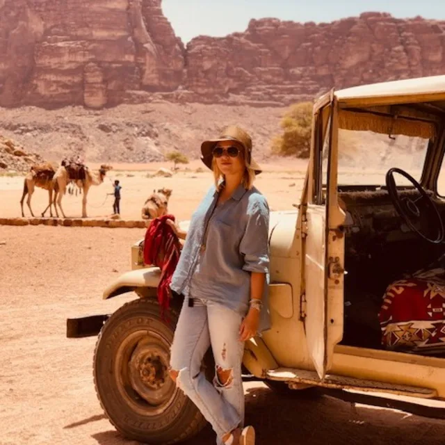 Travel Advisor Nicole Poff in front of a yellow car with camels and mountains in the background.