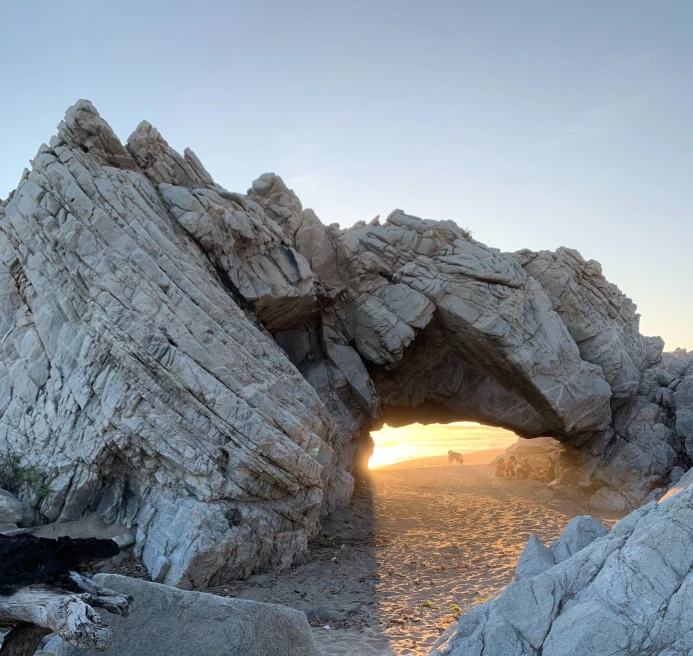 rock formation on a beach with a sunset peaking through an an arch