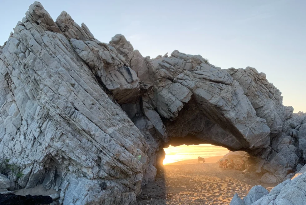 rock formation on a beach with a sunset peaking through an an arch