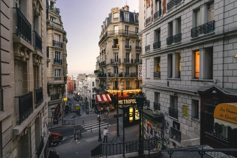 Street in Paris France with lit shops, white buildings and red yellow store fronts at sunset