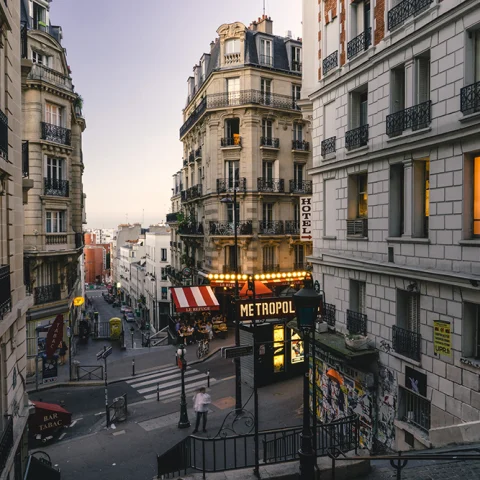 Street in Paris France with lit shops, white buildings and red yellow store fronts at sunset