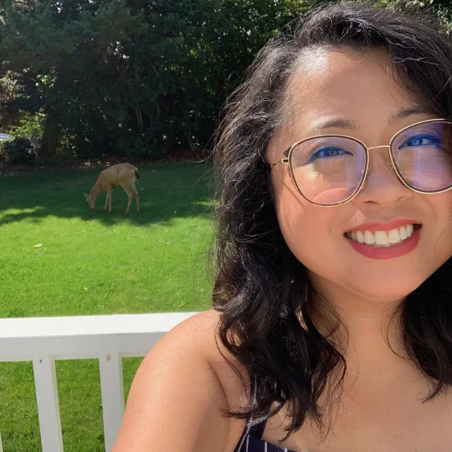 Travel advisor Jennyl Calugas wears a striped navy and blue top and smiles in front of a backyard with a dog in the grass