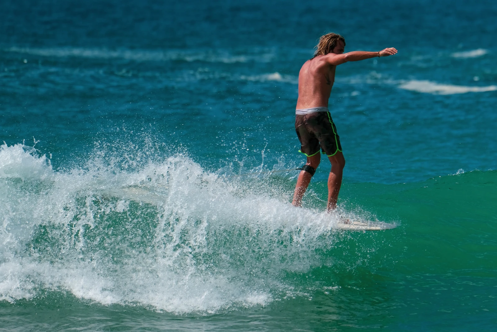 A surfer with brown swim shorts riding a blue and white wave on a white surfboard in Sri Lanka.