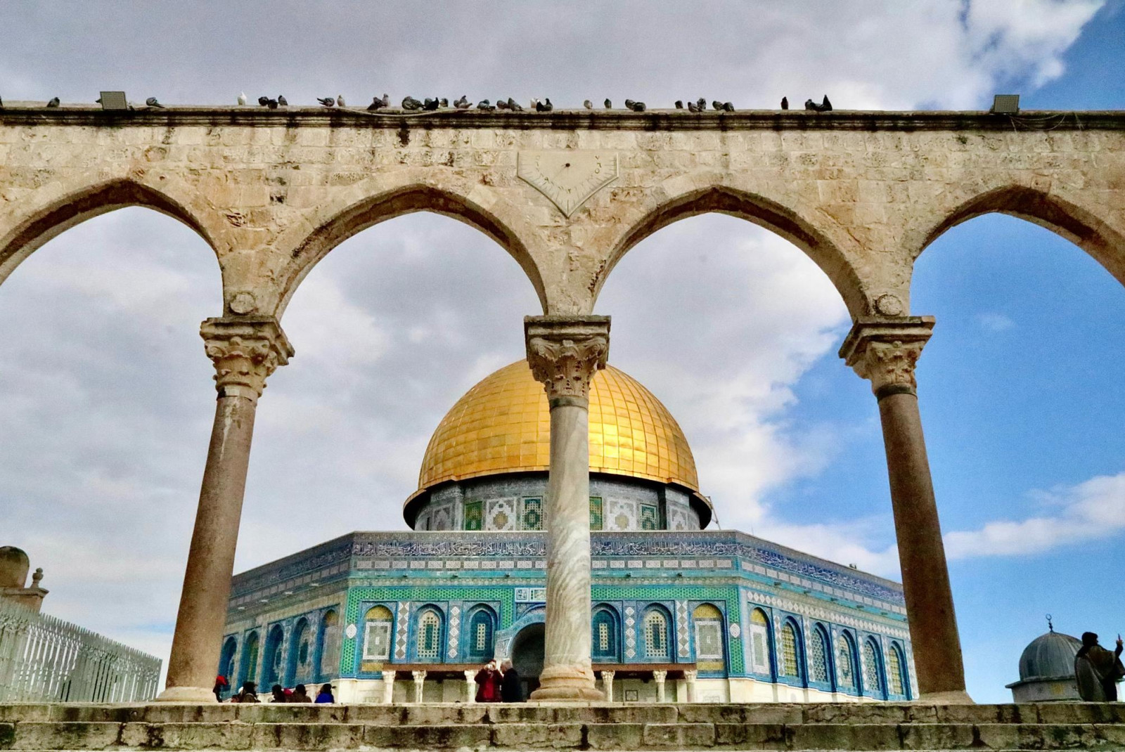Temple Mount with golden dome with stone arches in front on a sunny day.